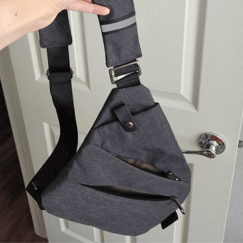Front view of the grey Anti‑theft Travel Bag held by strap, showcasing its compact triangular shape, hidden zip pocket, and crossbody design.