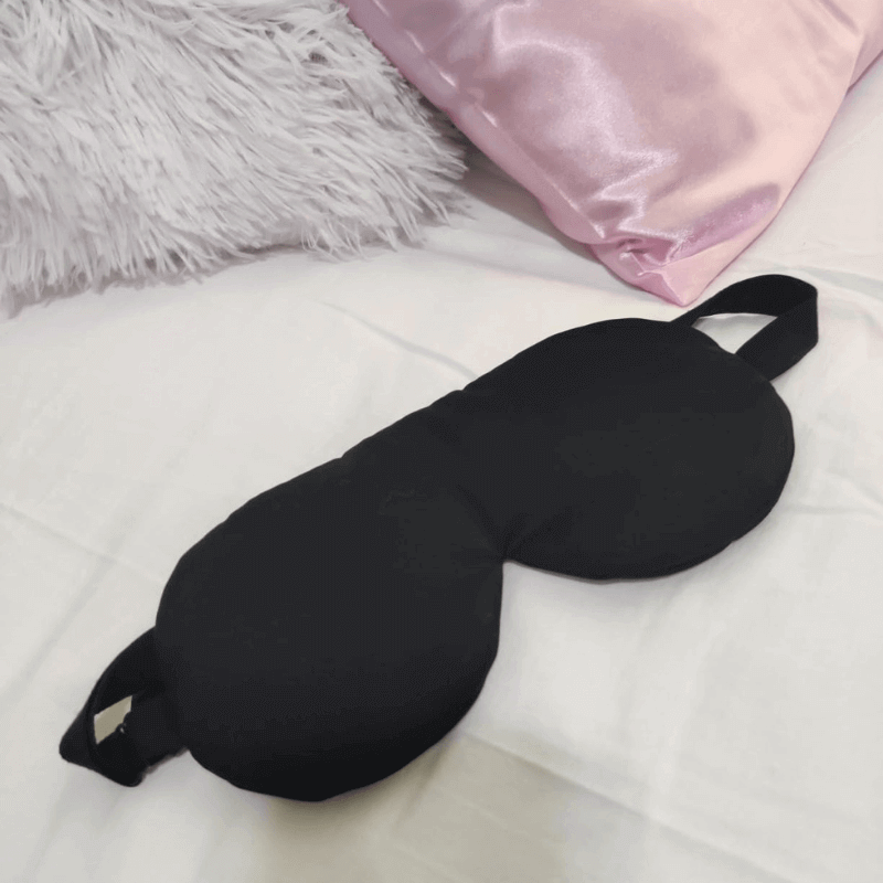 Natural silk sleep mask displayed flat on a white bed, showing its smooth texture and adjustable strap.