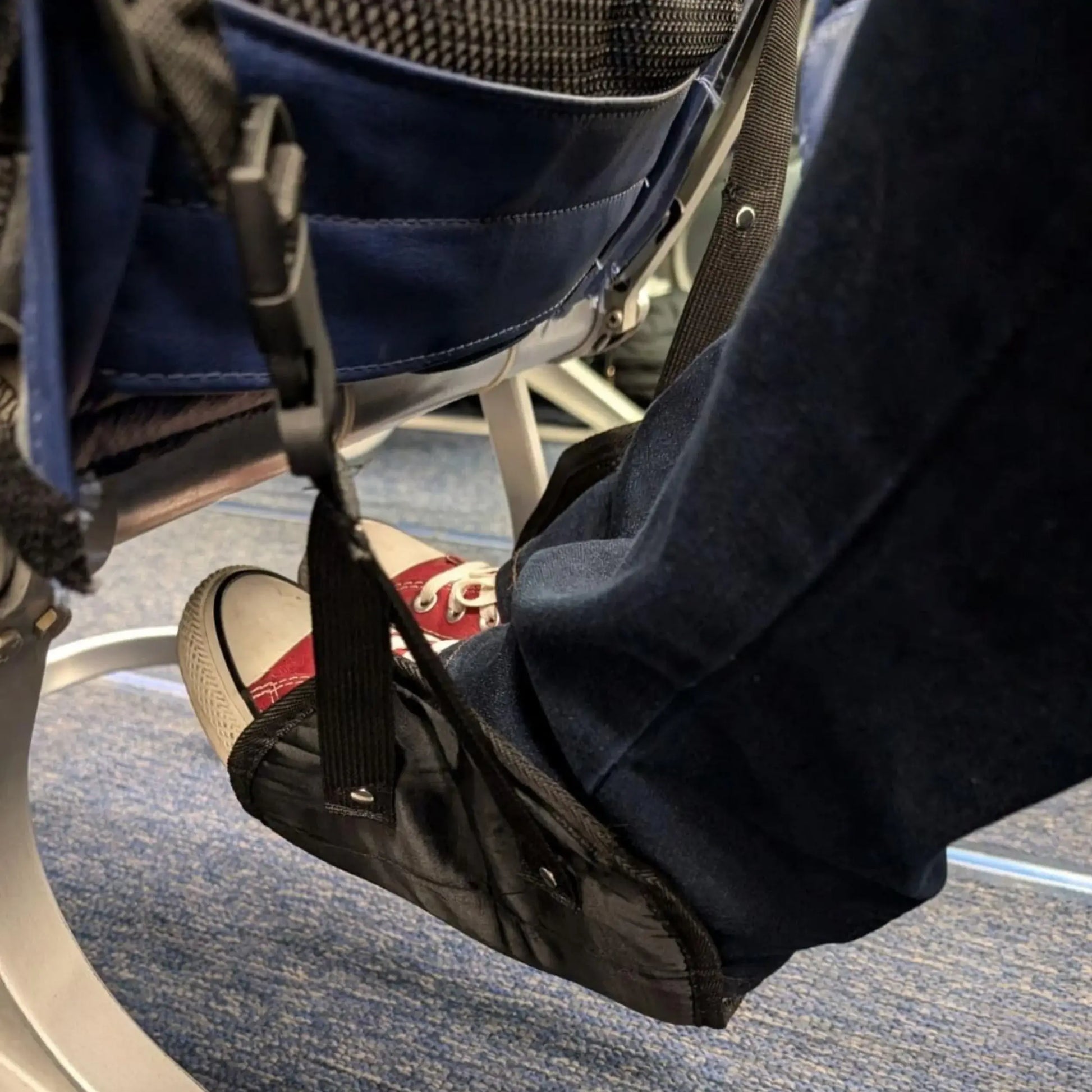 Passenger using a black airplane footrest while seated on a plane to elevate legs and increase comfort during flight.