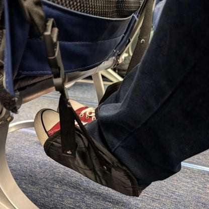 Passenger using a black airplane footrest while seated on a plane to elevate legs and increase comfort during flight.